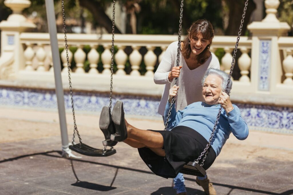 Mujer mayor es columpiada por una cuidadora en el parque