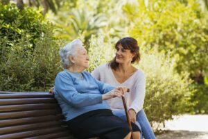 Una cuidadora y una anciana están sentadas en un banco de un parque