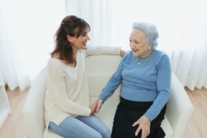Una mujer mayor está sentada en un sillón junto a su cuidadora