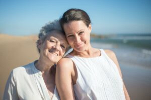 Mujer de mediana edad junto a mujer mayor en la playa: poniendo en práctica el cuidado holístico al fomentar la actividad