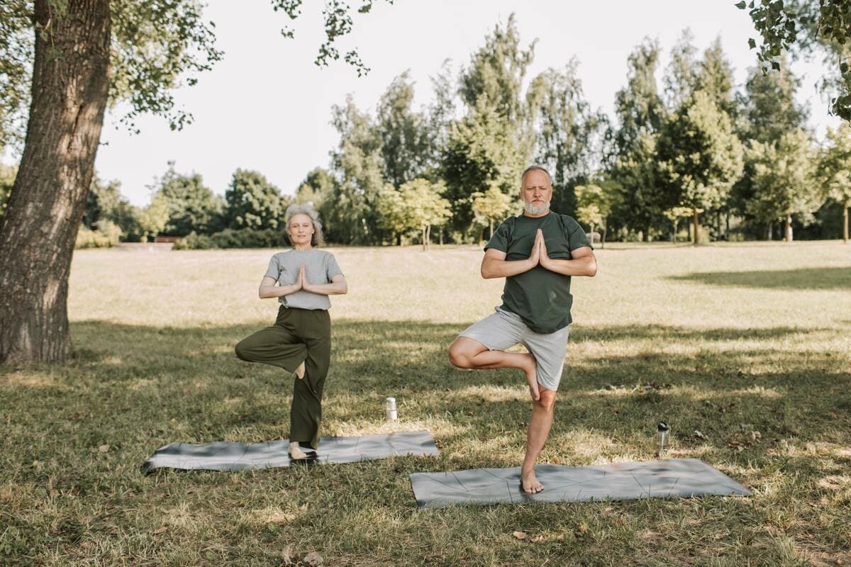 Dos personas mayores practicando yoga en un parque