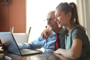Una cuidadora le enseña a un anciano a utilizar el ordenador: una buena forma de fomentar la actividad en la vejez