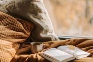 Bodegón de manta, café y libro junto a una ventana