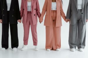 4 mujeres vestidas con trajes anchos de colores se cogen de las manos. No se les ve la cabeza