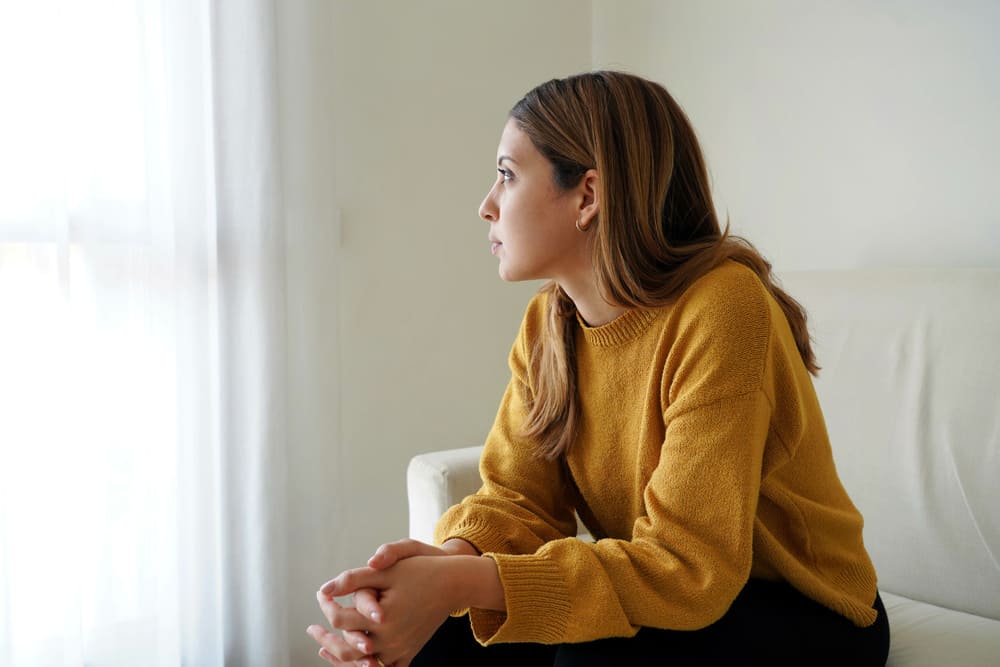 Una chica joven con semblante triste mirando a la nada en su sofá.